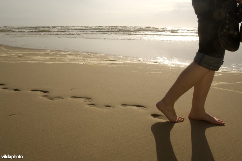 Een vrouw loopt op blote voeten over het strand