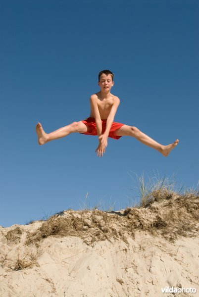 Jongen springt van een duin